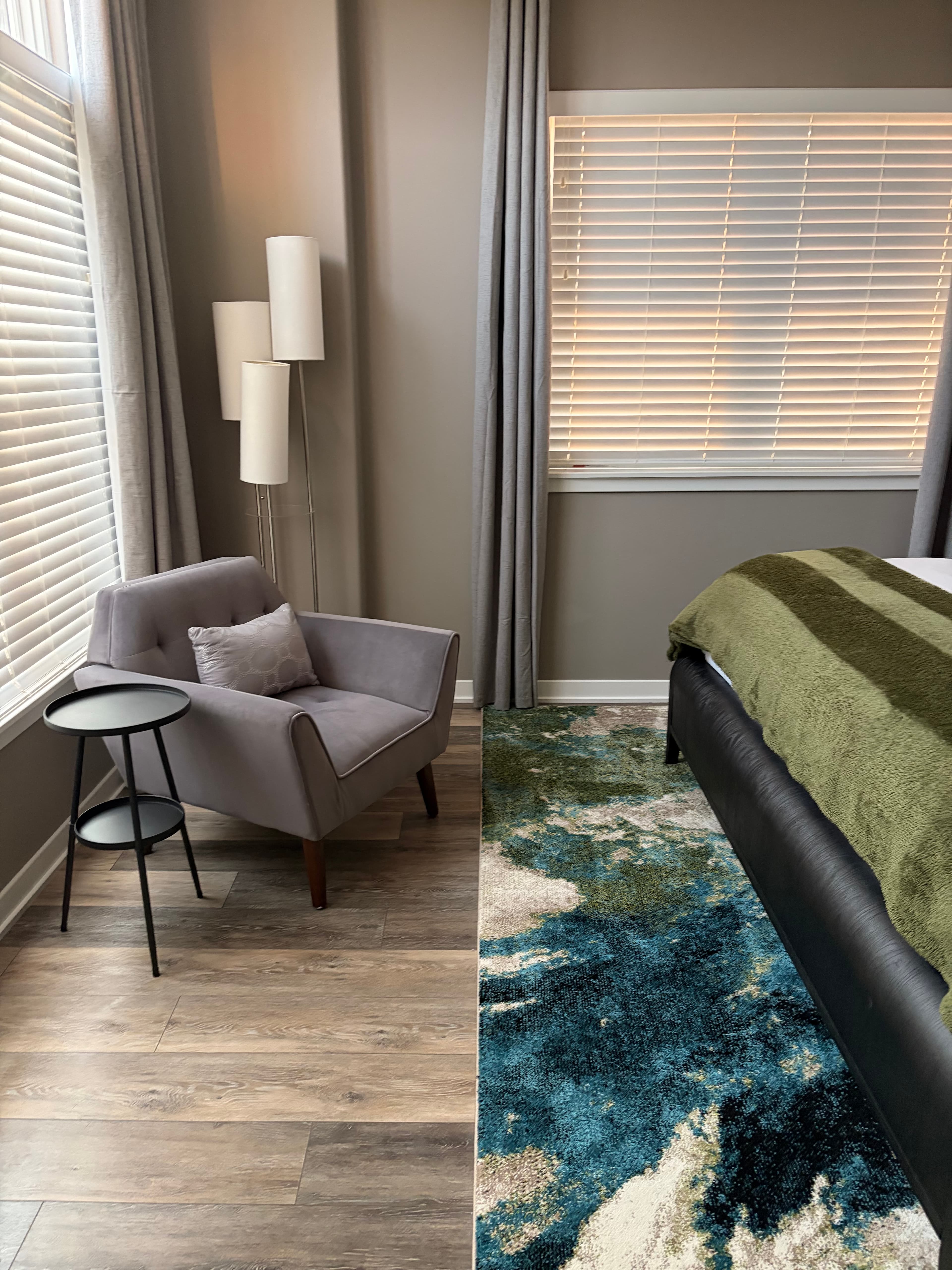 Modern bedroom corner featuring a grey armchair, black side table, and a blue patterned rug.