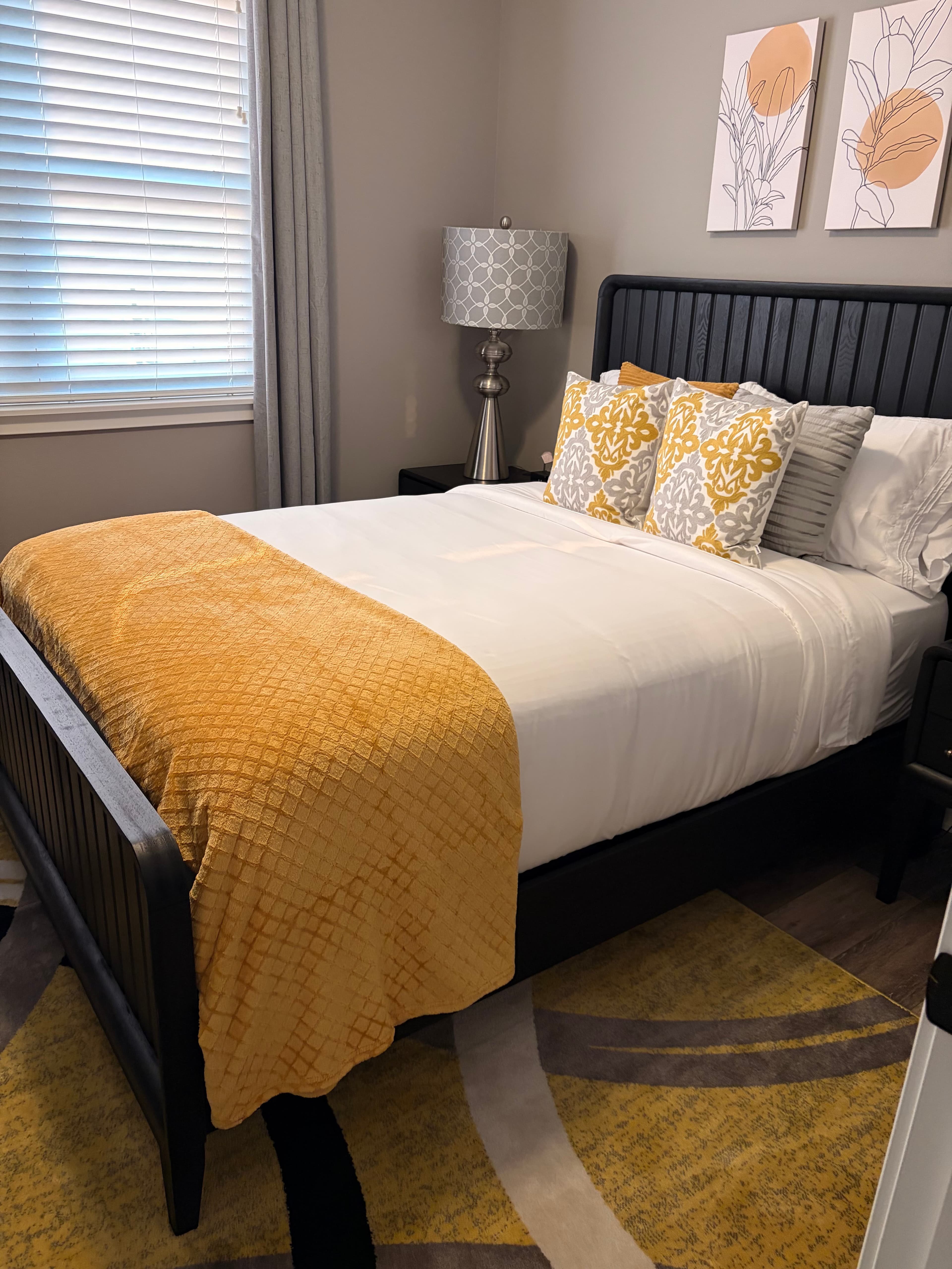 Modern bedroom with a black bed, yellow throw, patterned pillows, and abstract botanical wall art.
