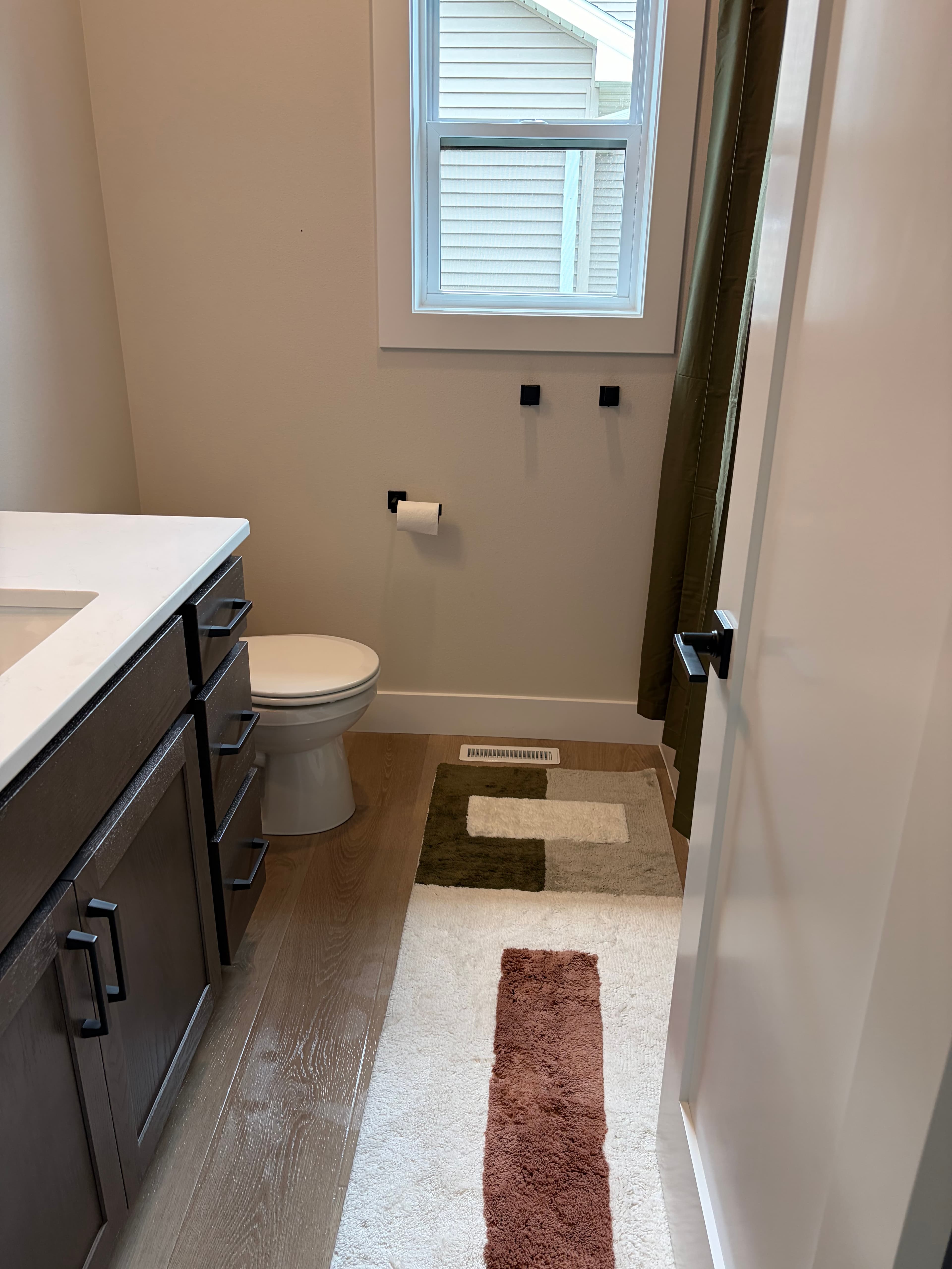 Modern bathroom with dark wood vanity, white toilet, and a long geometric patterned runner.