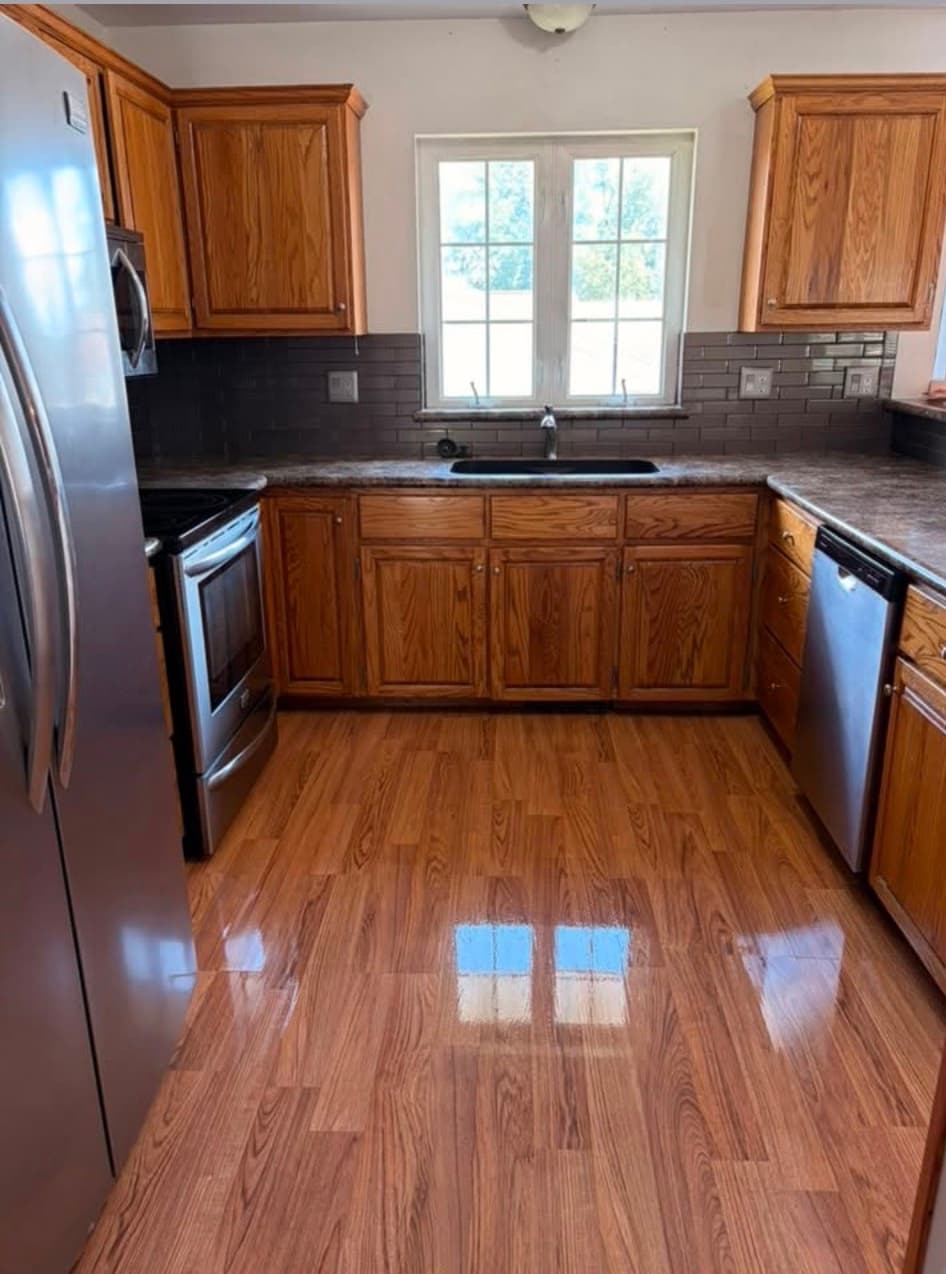 Kitchen featuring oak cabinets, dark grey backsplash, stainless steel appliances, and shiny wood-look flooring.