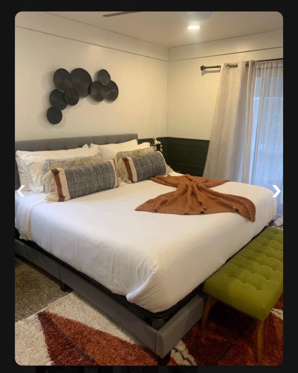Modern bedroom with white bedding, rust throw, green bench, and black circular wall art.