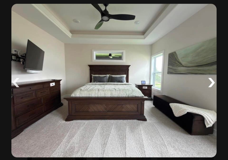 Spacious bedroom with dark wood furniture, a mounted TV, abstract art, and a ceiling fan.