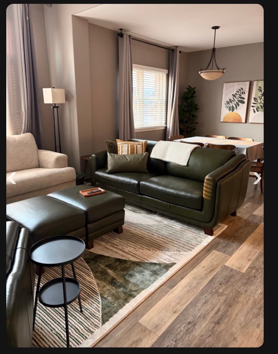 Modern living room featuring a dark green leather sofa, patterned rug, and adjacent dining area.